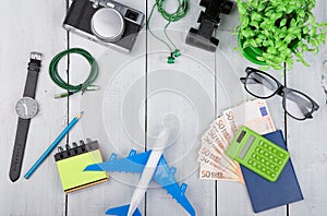 plane, passport, money, camera, headphones, binoculars, watch, calculator, eyeglasses on white wooden table