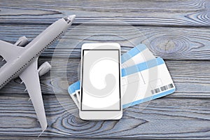 Plane, tickets, smartphone with a white screen on a wooden background.