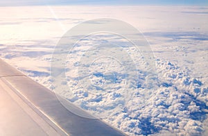 Plane window view of a wing and clouds in the sky