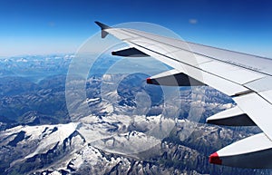 Plane wing over Alps with snow on mountains summer