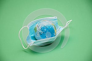 planet earth in the form of a ball and face protection medical mask on a green background