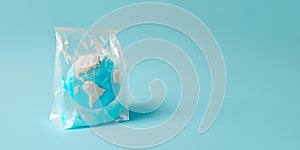 Planet earth in plastic bag on bright pastel blue background. Minimal creative concept of dystopian future. Climate change or