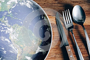 The planet Earth plate with a fork and knife on a wooden background. World hunger concept. Feed the world photo