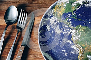 The planet Earth plate with a fork and knife on a wooden background. World hunger concept. Feed the world