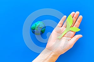 Planet, ecology. plastiline symbol of planet Earth globe and plant coutout on blue background top view copy space