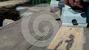 Planing an old board with an electric plane in sunlight. Refresh the wood plank surface