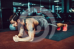 Muscled young man wearing sport wear and doing plank position while exercising on the floor in loft interior