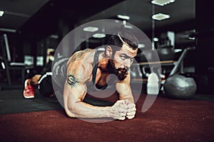 Muscled young man wearing sport wear and doing plank position while exercising on the floor in loft interior