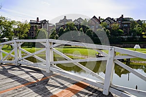 Planked footbridge over lake before houses in sunny autumn after