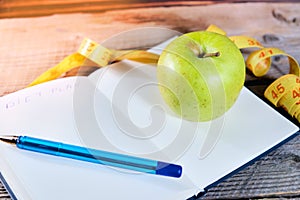 Planning of a diet. A notebook c an inscription - the Diet, a measuring tape, an apple and pen