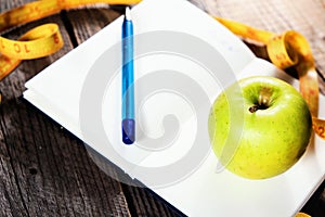 Planning of a diet. A notebook c an inscription - the Diet, a measuring tape, an apple and pen