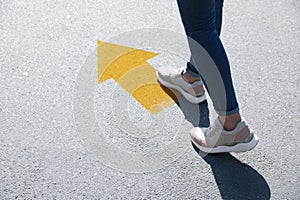 Planning future. Woman walking to drawn mark on road, closeup. Yellow arrow showing direction of way