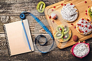 Planning healthy diet concept. Workout and fitness dieting. Fruits toasts, measuring tape and empty notebook on wooden background