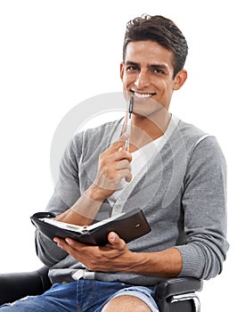 Planning keeps him punctual. Portrait of a handsome young man sitting with diary in hand and smiling against a white