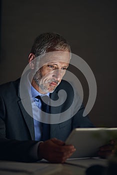 Planning late into the night. a mature businessman using a digital tablet while working late in an office.