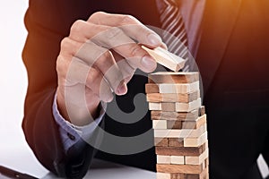 Planning, risk and strategy in business concept, businessman gambling placing wooden block on a tower