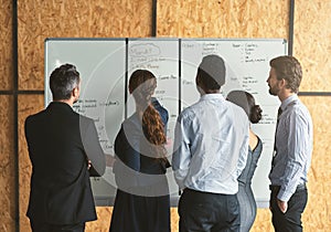 Planning the way forward. Rearview shot of a group of businesspeople looking over plans on a whiteboard.