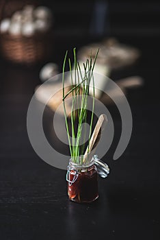 Tarro de cristal lleno de mermelada de fresa y cebollino con cuchillo de madera sobre mesa negra photo