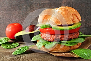 Plant based meatless burger with avocado, tomato and spinach against a dark background