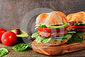 Plant based meatless burgers with avocado, tomato and spinach against a dark background