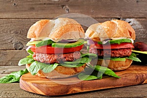 Plant based meatless burgers with avocado, tomato and spinach against a wood background