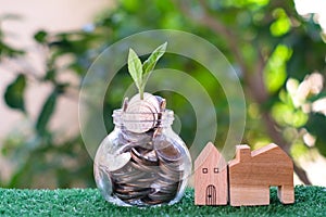 Plant growing from coins in glass jar. Wooden house model on artificial grass. Home mortgage and property investment concept