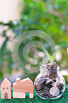 Plant growing from coins in glass jar. Wooden house model on artificial grass. Home mortgage and property investment concept