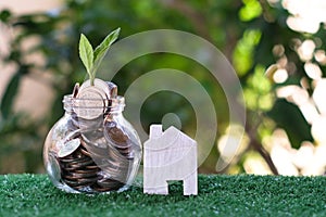 Plant growing from coins in glass jar. Wooden house model on artificial grass. Home mortgage and property investment concept