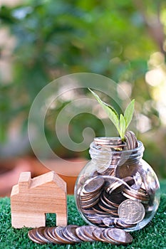 Plant growing from coins in glass jar. Wooden house model on artificial grass. Home mortgage and property investment concept