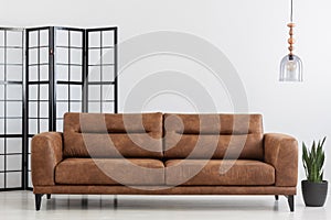 Brown leather sofa in white simple living room interior. Real photo