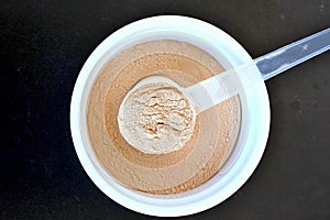 Plant protein powder from rice a pea in white bowl with plastic spoon on black background
