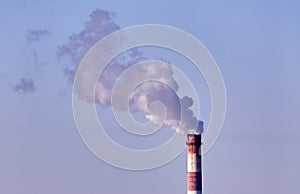 The plant\'s tall brick chimney emits a long cloud of thick white smoke against a blue sky