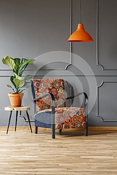 Plant on table next to patterned armchair under orange lamp in g
