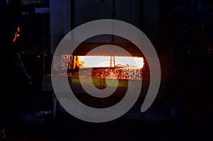 The plant worker hardens the metal in a huge red-hot furnace in the production workshop of the plant