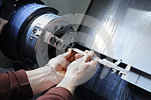 At the plant. Workers hands checking dimensions of part fixed in the spindle of the lathe using calipers