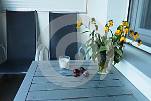 Plants and flowers of Jerusalem artichoke in a vase. Chestnut fruits on the table. Table and chairs on the balcony or