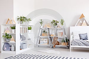 Plants on shelves in scandi grey bedroom interior with striped c