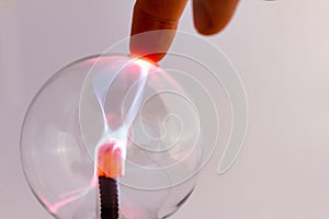 Plasma lamp on neutral background. Fingers of a man attracting the luminous electric flow. Crystal ball with electricity and light