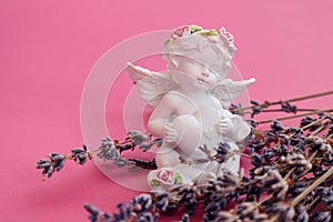 Plaster angel figurine with a heart with lavender branches on a pink background, side view, space for text