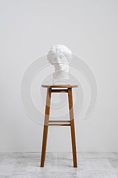 Plaster head, antique sculpture for learning to draw. Standing on a stool on a white background.