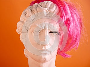 Plaster head of statue with pink wig and eyelashes. Man and  woman in half. Concept of gender identity