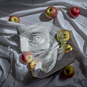 Plaster marble copy eye of david against a background of white drapery fabric with folds with green pears and red apples in light