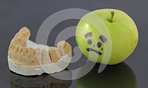 Plaster model of lower teeth next to crying green apple