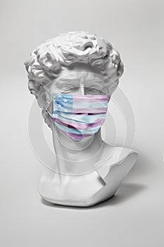 Plaster statue of David's head in medical mask with print of USA flag. Minimal concept photo.