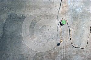 A Plaster Wall with Cracks and Paint Spots in the Workshop with Old Green Electric Plug Socket and Hanging Wires and a Plug