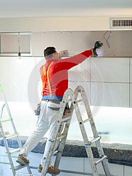 Plasterboard worker installs a plasterboard wall on the kitchen cabinets to cover the extractor pipe of the hood