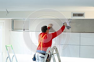 Plasterboard worker installs a plasterboard wall on the kitchen cabinets to cover the extractor pipe of the hood