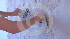 Plasterer man aligning wet plaster on wall using long metal spatula, closeup.