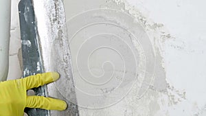 Plasterer man holding putty knife is spackling patching a hole in white wall.