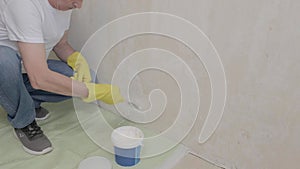 Plasterer man holding putty knife is spackling patching a hole in white wall.